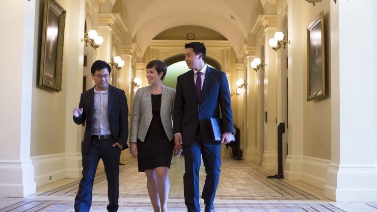 Three students dressed in suits walk through a hallway of the California State Capitol.