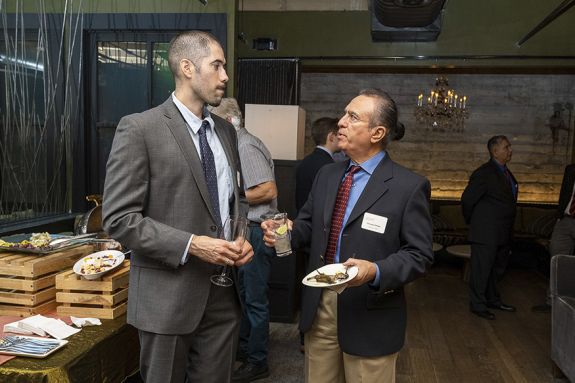 Two Latinx individuals stand talking at an event.