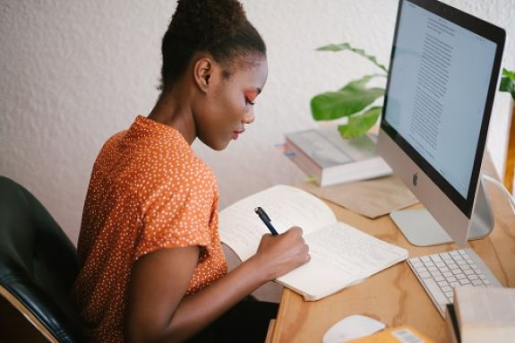 A student writing notes in front of a laptop