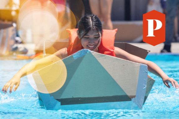 Student paddling on a cardboard boat in the pool