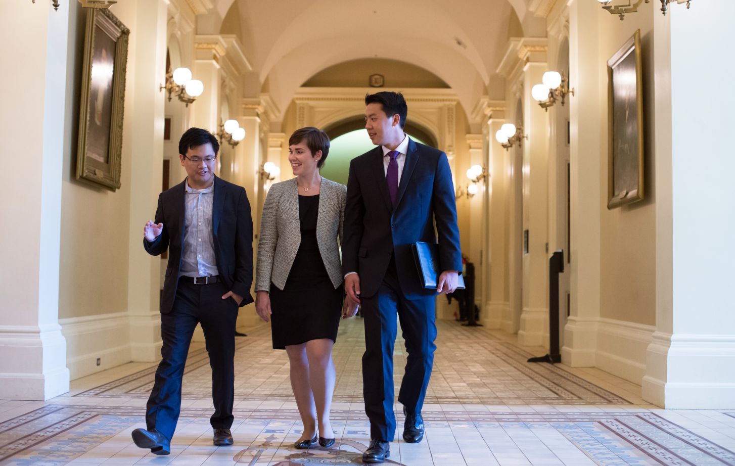 Three students dressed in suits walk through a hallway of the California State Capitol.