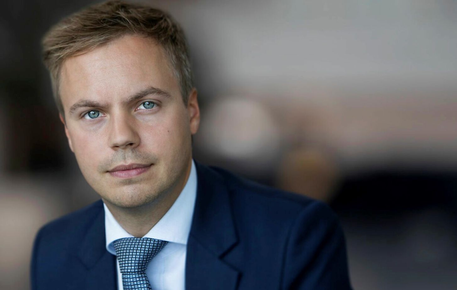 A man in a suit poses for a photo in front of a blurred background