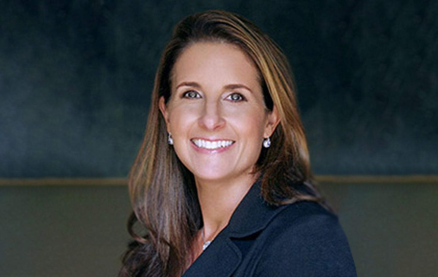 A headshot of a brunette woman in front of a blue background