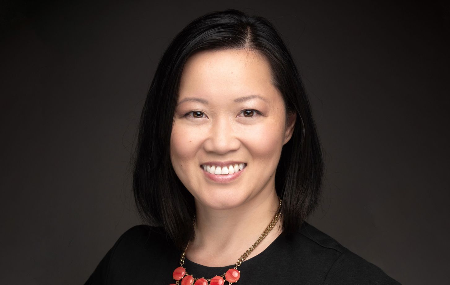 A headshot of an Asian woman in a black shirt, in front of a neutral background