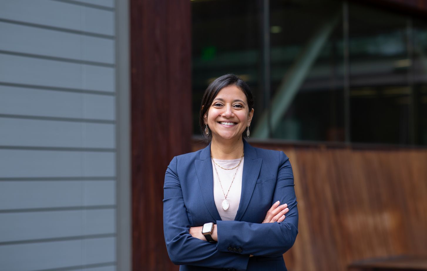 A woman in a navy suit poses smiling, with her arms crossed.
