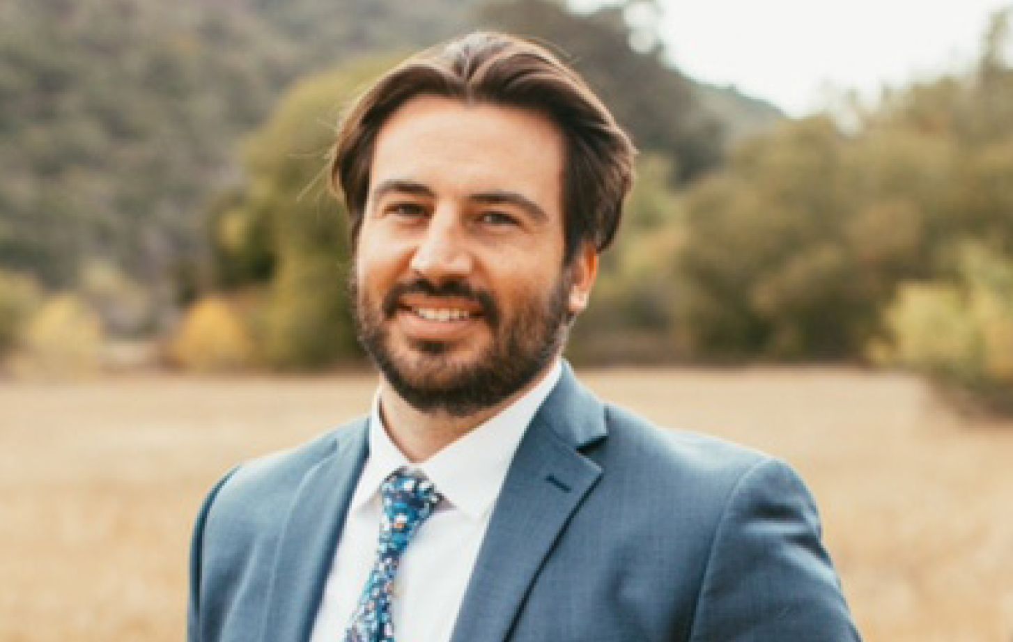 A man wearing a suit smiles for a photo outdoors