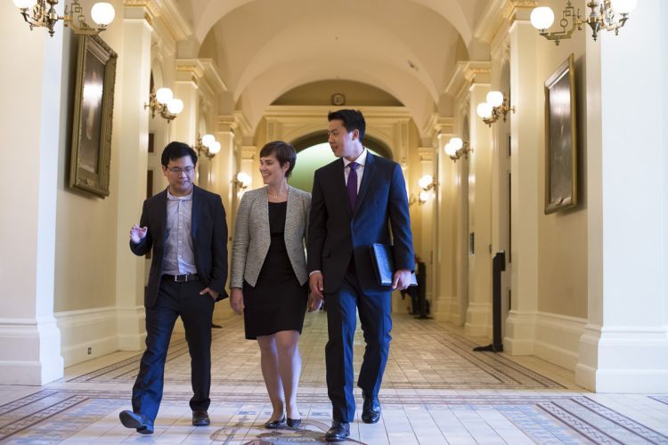 Three students dressed in suits walk through a hallway of the California State Capitol.