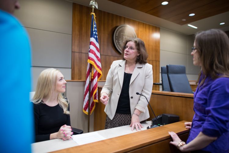 A female teacher talks to three students in a courtroom