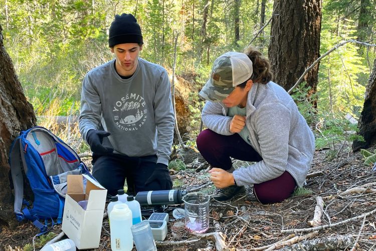 Students sitting in field with materials for collecting water samples.