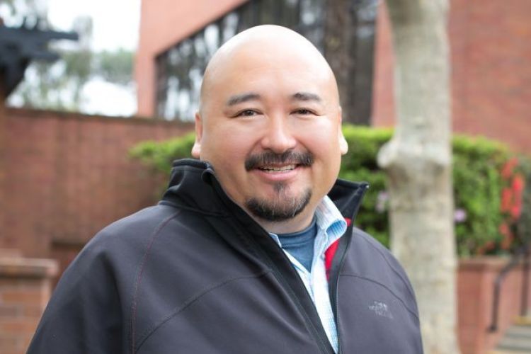 A man poses outside a campus building for a photo.