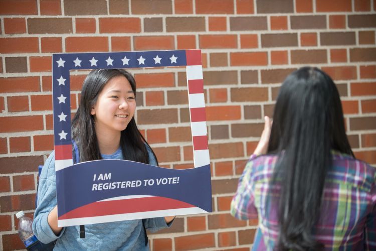 A student holds a sign reading "I am registered to vote" while someone takes a picture