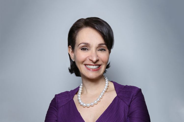 A smiling woman in a purple dress poses with her arms crossed.