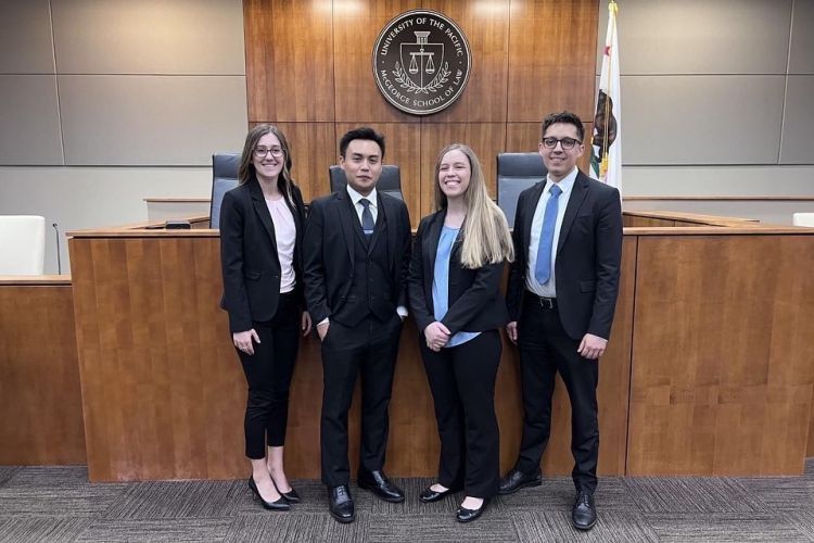 Four students pose for a photo in a courtroom