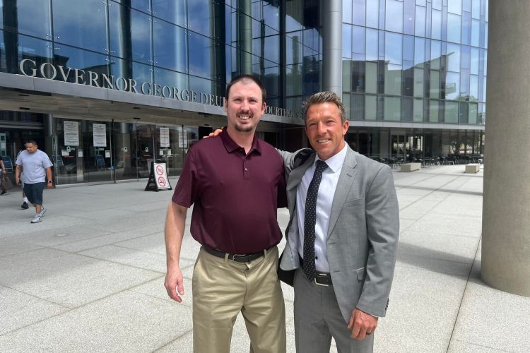 Two men pose for a photo in front of a courthouse