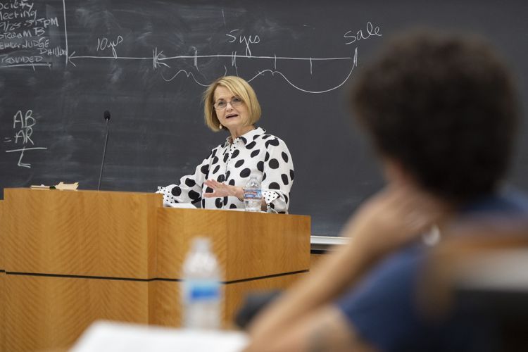 A female professor behind a podium speaks to a classroom of students