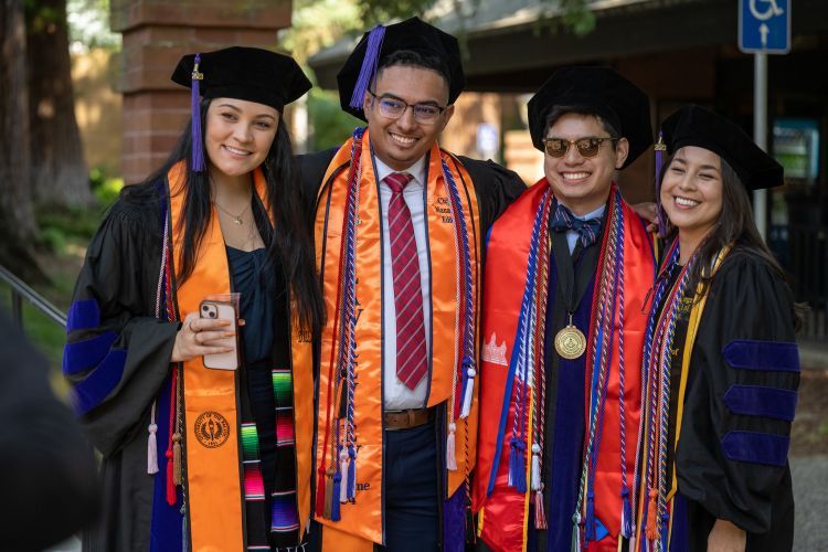 Four graduates wearing regalia pose for a photo