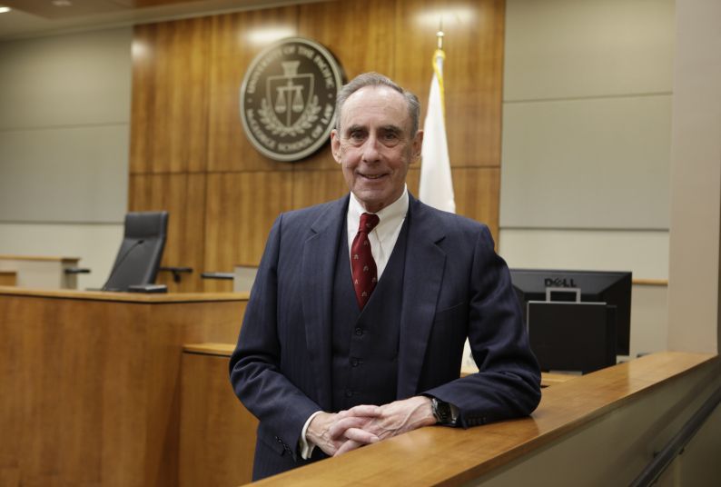 A man in a suit poses for a photo in a courtroom.