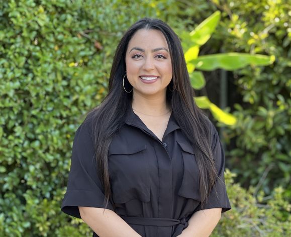 A woman wearing a black dress smiles for a photo outside