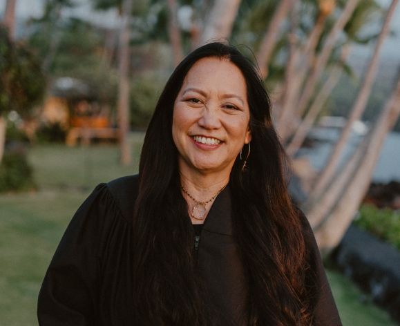 A female judge wearing a robe smiles for a photo outside