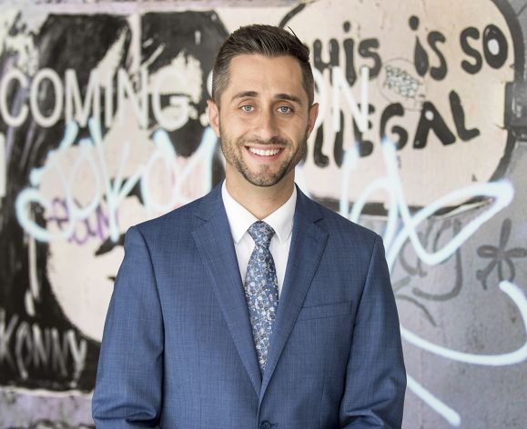 A man wearing a suit smiles for a photo in front of a graffiti wall