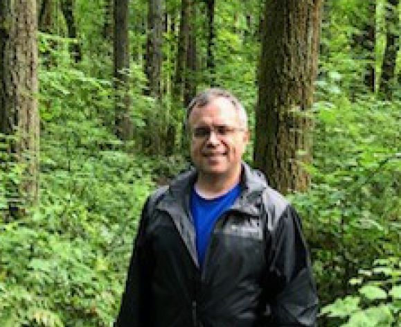 A man outdoors in the woods smiles for a photo